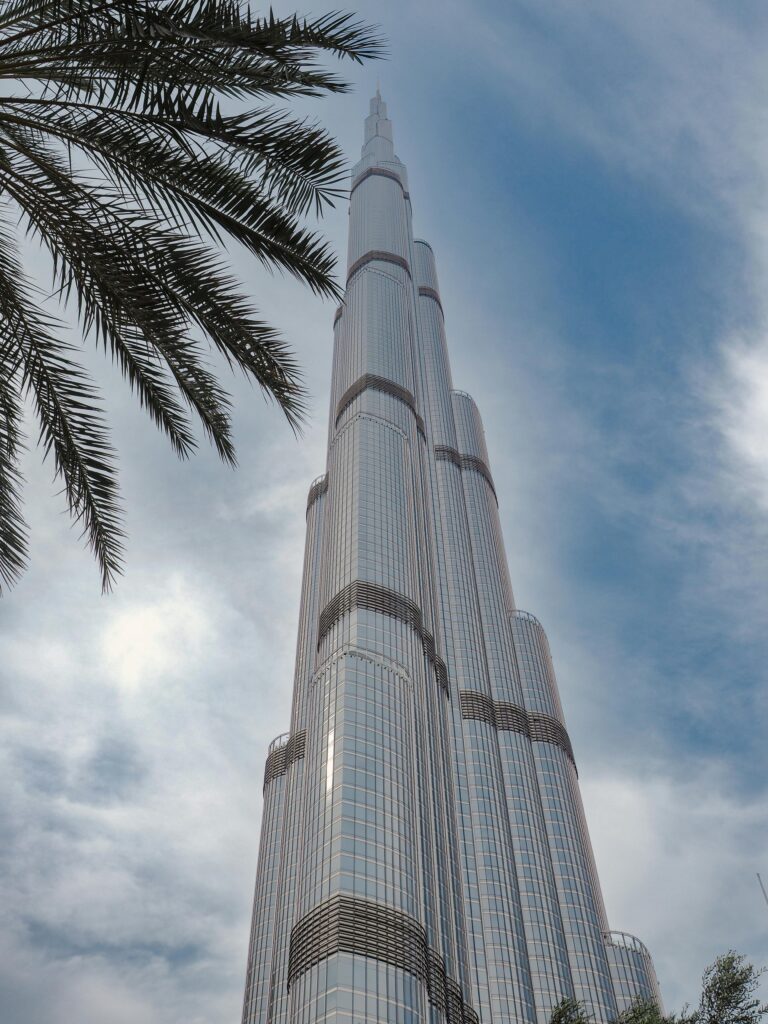 The iconic Burj Khalifa seen from below, against a blue sky with palm branches.